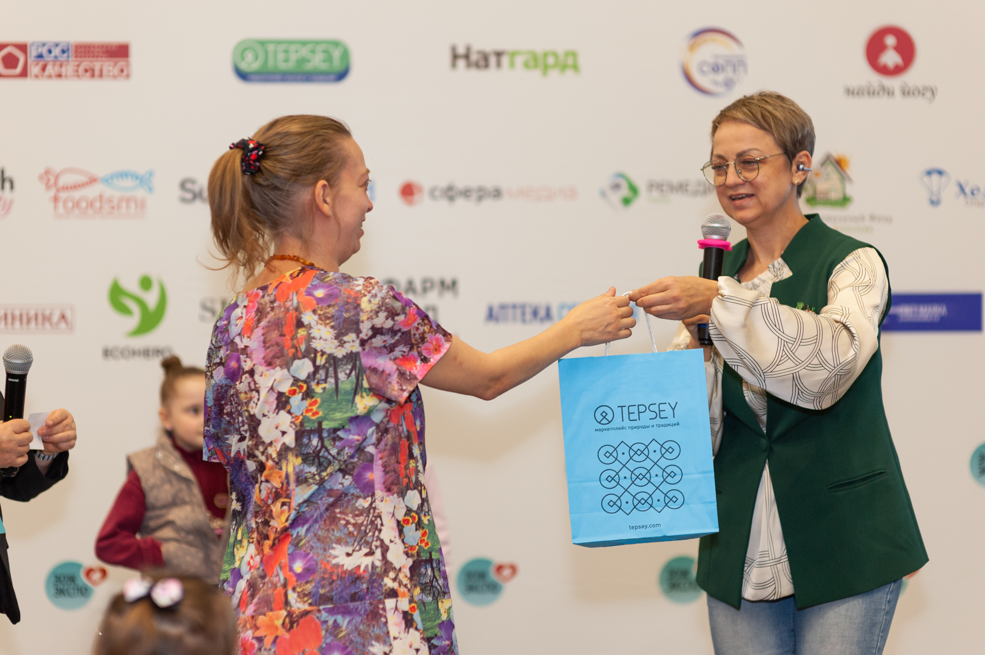 Участнице вручают голубой фирменный пакет TEPSEY на розыгрыше